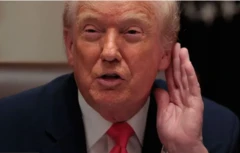 Трамп у синьому костюмі тримає руку біля вуха