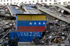 Um muro onde estava pintada a bandeira da Venezuela permanece destruído diante de um edifício que desabou após os terremotos em La Guaira, 26 de junho de 2026
