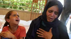 Umugore w'umunya Palestine n'umukobwa wiwe bagandaye inyuma y'aho umuhungu wiwe yiciwe ahatangirwa imfashanyo 