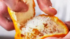 Close up de dedos descascando a casca de mexerica revelando a fruta por baixo