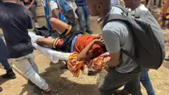 An injured man, in a brown shirt and black short, is carried on a stretcher