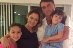 Jair Bolsonaro com Michelle Bolsonaro e as duas filhas. Michelle e Letícia sorriem olhando para a câmera, enquanto Bolsonaro está sério e Laura, em seu colo, morde o lábio inferior
