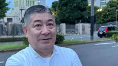 Homem sorrindo contidamente em pé perto da rua