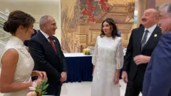 Şəklin sol tərəfində ağ geyimdə olan Anna Hakobyan görünür. Onun yanında Ermənistan Baş naziri Nikol Paşinyan dayanıb. Paşinyan gülümsəyir. Ondan sağda ağ geyimdə olan Mehriban Əliyeva dayanıb. Onun sağında isə İlham Əliyev dayanıb və o, gülür. 