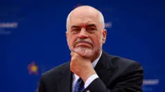 Edi Rama u crnom odelu i sa šarenom kravatom drži se rukom za podbradak i gleda u daljinu