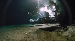 Un sumergible tripulado flota justo por encima de un oscuro lecho marino, rodeado de finos sedimentos.