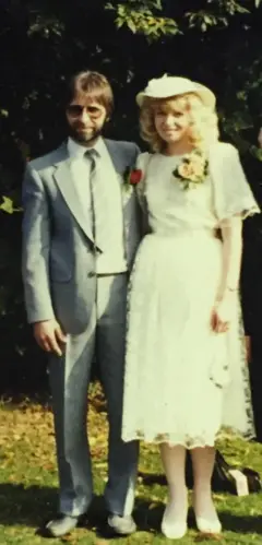 Dave Gilmore, de barba e óculos escuros dos anos 1980, de terno com Kate ao seu lado, de cabelo loiro e vestido de noiva