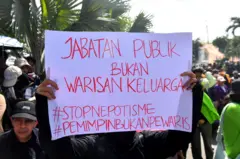 Seorang demonstran membentangkan poster protes bertuliskan jabatan publik bukan warisan keluarga.