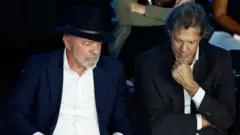 Lula e Haddad sentados olhando para baixo em silêncio.