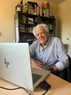 Juan López González olha sorrindo para a câmera, atrás de um notebook