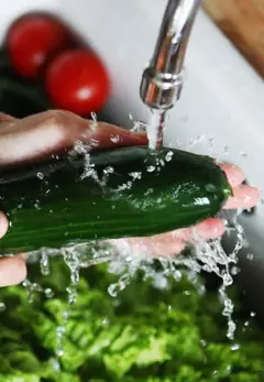 Uma mão lavando um vegetal na pia