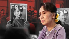 ကင်မရာရဲ့ အဝေးဘက် တစ်ဖက်ခြမ်းကို ငေးကြည့်နေတဲ့ ဒေါ်အောင်ဆန်းစုကြည်၊သူ့နောက်မှာ သူ့ကိုလွှတ်ပေးဖို့တောင်းဆိုနေတဲ့လူတွေက ဆိုင်းဘုတ်ကိုင်ထားတဲ့ အနီရောင် အဖြူရောင် အနက်ရောင် ပေါင်းစပ်ဓာတ်ပုံဖြစ်ပါတယ်၊​