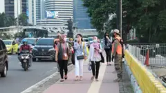 Pekerja di Jakarta sedang berjalan di sepanjang jalan sambil mengenakan pelindung wajah dan masker.