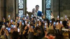 Marianela Núñez acena de uma janela do Teatro Colón, em Buenos Aires, para seu público, que tira fotos dela com seus celulares.