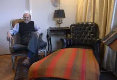 Un hombre sonriente sentado en un sillón, al lado de un diván de psicoterapia