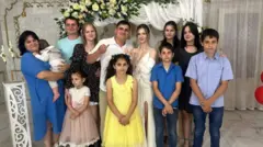 ヴォロノフ一家の12人がカメラに向かって並んでいる。大人たちは、笑顔を見せている。結婚指輪をはめた指を見せる新郎新婦とみられる男女が中央に立ち、両隣に複数の男女、前に男の子と女の子が立っている