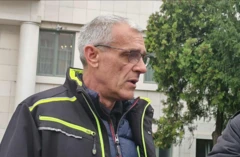 Sedi muškarac u tamnoj jakni sa svetlo zelenim detaljima gleda u stranu