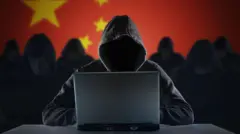 ጥቁር ሹራብ የለበሰ ፊቱ የማይታይ ጠላፊ ኮምፒውተር ፊት ለፊት ተቀምጦ፤ ከኋላም የቻይና ሰንደቅ ዓላማ ይታያል