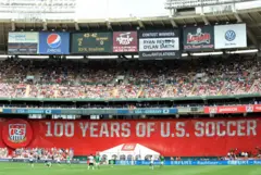 Jogo de futebol com um placar vermelho gigante no estádio em comemoração aos 100 anos da U.S. Soccer. O placar eletrônico mostra Estados Unidos 2x0 Alemanha, ao lado de publicidade de várias empresas.