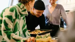 Homem e duas mulheres sorrindo e cozinhando