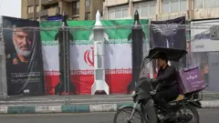 Автомобилист проезжает мимо макетов иранских ракет, установленных вдоль дороги на площади Валиаср в Тегеране 22 марта 2026 года.