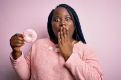 Une femme tient un beignet et se tient la bouche