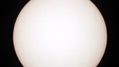 Uma foto do Sol o mostra como um grande disco branco e, na extremidade esquerda, um diminuto ponto preto, que é Mercúrio