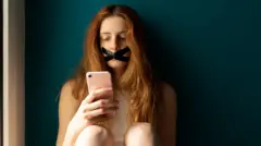 Una mujer joven con la boca tapada usando un teléfono móvil.