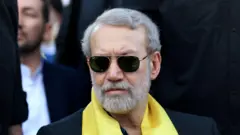 Секретарь Высшего совета национальной безопасности Ирана Али Лариджани, седой бородатый мужчина в темных очках и желтым шарфом на шее, принимает участие в церемонии, организованной "Хезболлой" в память о первой годовщине убийства Хасана Насраллы Израилем, на окраине Бейрута, Ливан, 27 сентября 2025 года