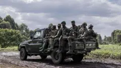 Abarwanyi ba M23 bicaye mu modoka ifunguye inyuma irimo kugenda 