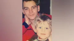 Foto de família mostrando Fred May-Davis com a mão no pescoço e seu filho Jack no colo