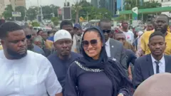 Senator Natasha Akpoti-Uduaghan [second left] wear all black wit white crystal design as some men wey look like her supporters surround her.