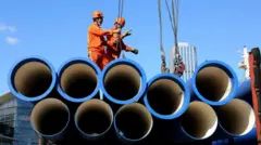 Dois trabalhadores portuários em cima de dutos no porto de Lianyungang, província de Jiangsu, no leste da China