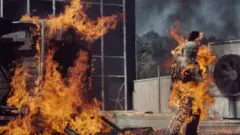 Kitty O'Neill camina por un lote envuelto en llamas durante una de sus acrobacias.