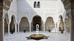 A courtyard with tiled floor, fountain and white ornately carved walls