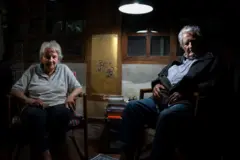 Lucía Topolansky e José Mujica sentados em cadeiras na sala de casa