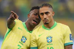 Vinicius Jr. (esq.) e Raphinha (dir.), com a camisa da seleção brasileira, conversam no campo de jogo