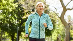 Mujer rubia madura trotando por la mañana en un parque público. Viste ropa deportiva.