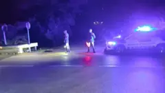 Dos efectivos de los servicios de asistencia están parados en una carretera cerca de un vehículo con sus luces de emergencia encendidas