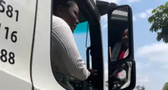 Ifoto igaragaza umushoferi w'umugore atwaye ikamyo. Yambaye umupira w'umweru w'amaboko maremare, imbere harimo umupira utukura.