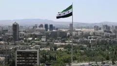Şam'daki bir tepeden şehir manzarası ve Suriye'de yeni yönetimin bayrağı görülüyor.