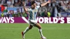 白と水色の縦じまのユニホームを着た選手が、ピッチ上で両手を広げて笑顔で走っている