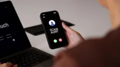 Una persona sostiene un teléfono inteligente que muestra un mensaje de “Alerta de estafa” en la pantalla