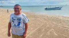 Pescador com o mar e barco de pesca ao fundo