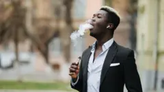 Ọkunrin to wọ aṣọ dudu ati funfun to n mu siga