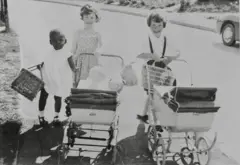 Na imagem, ela tem cerca de 4 anos e aparece ao lado de duas meninas que empurram carrinhos de boneca.