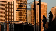 Pessoas passeiam tomando bebida em meio a prédios em uma cidade