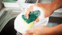 Unas manos lavando un plato con una esponja bajo un grifo de agua
