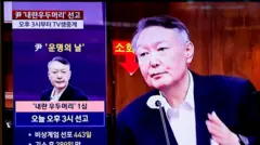 Женщина проходит мимо экрана, на котором транслируется суд. Камера показывает лицо Юна Сок Ёля, выступающего с последним словом.