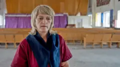 Tetyana Potapenko, une femme blonde d'âge moyen, a l'air pensif dans une salopette de prison marron. 